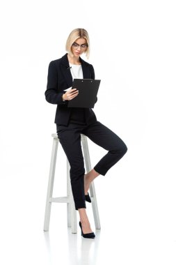 Haber sunucusunun tam boy görünümü beyaz pano ile yüksek taburede oturuyor