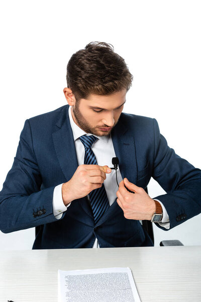 anchorman fixing microphone on blazer near paper with text on desk isolated on white