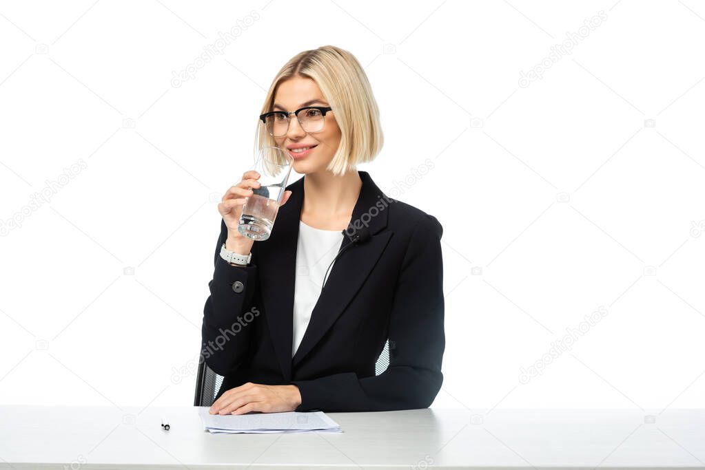 smiling blonde news anchor drinking water at workplace isolated on white
