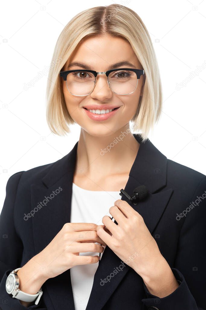 cheerful news presenter looking at camera while fixing microphone on blazer isolated on white