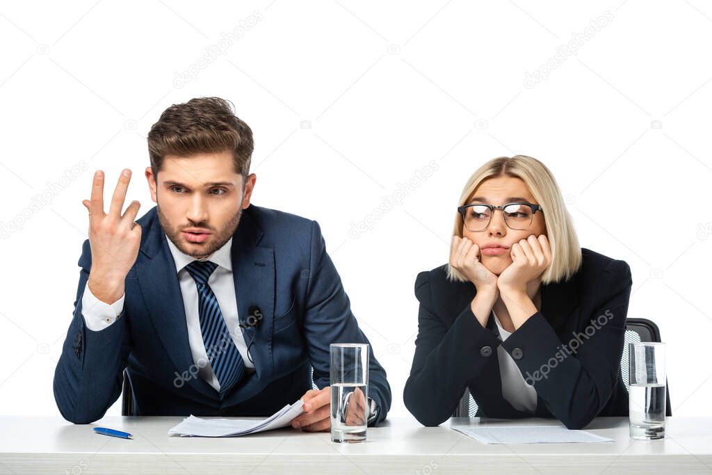 discouraged broadcaster gesturing near upset colleague at workplace isolated on white