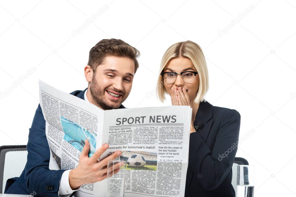 smiling news anchor showing newspaper to amazed colleague isolated on white