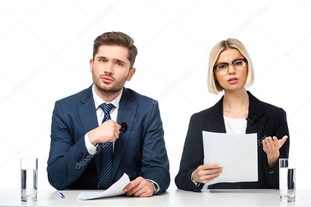 displeased news anchor holding paper and pointing with hand near colleague isolated on white