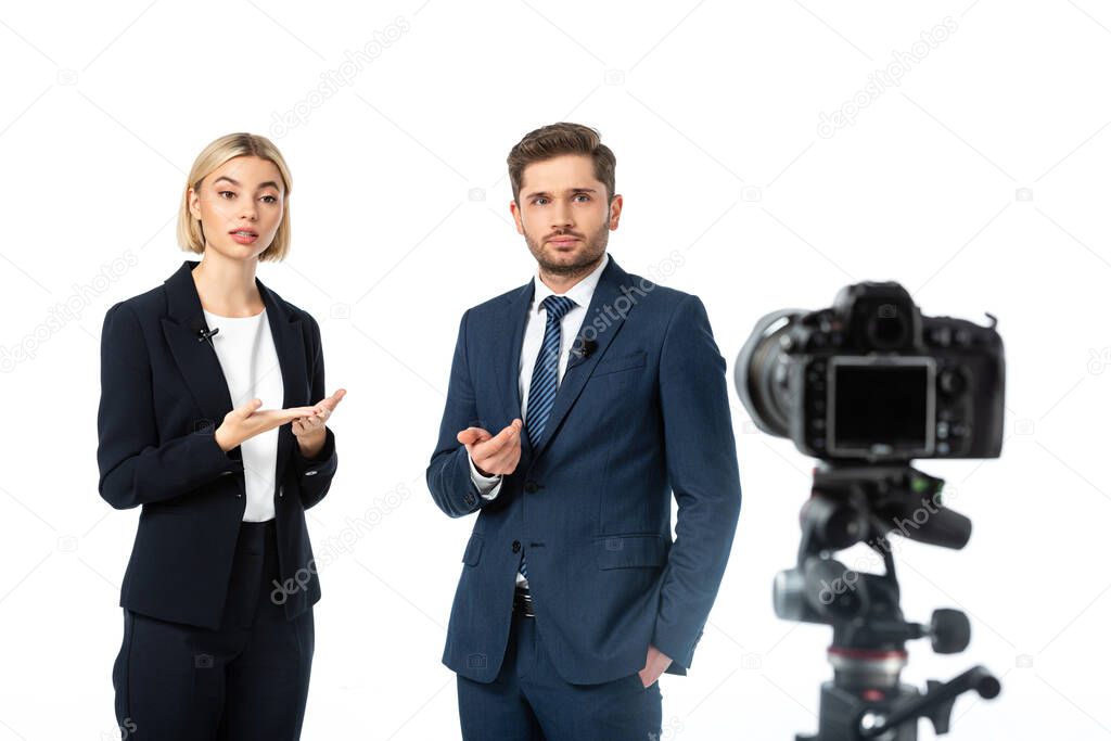 couple of news anchors working near digital camera on blurred foreground isolated on white