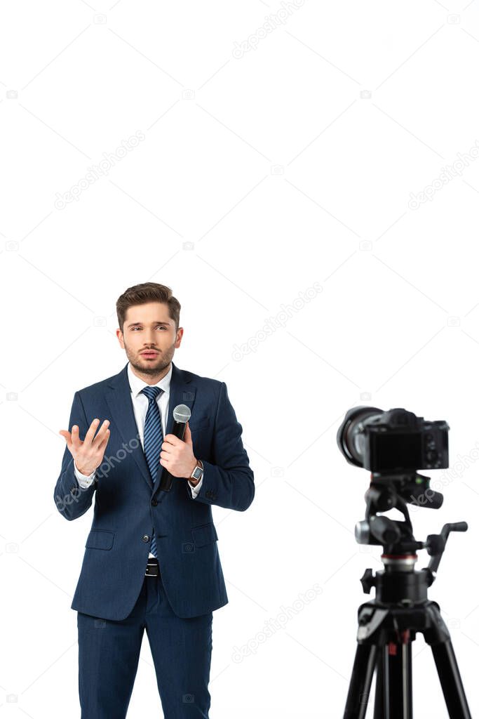 news commentator with microphone gesturing while talking near digital camera on blurred foreground isolated on white