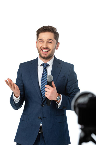 smiling journalist with microphone pointing with hand isolated on white, blurred foreground
