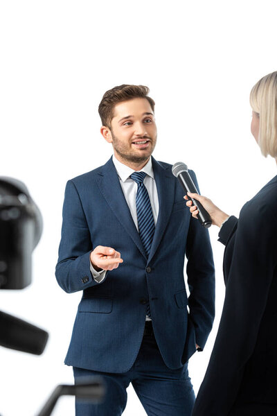 smiling businessman pointing with finger during interview with anchorwoman isolated on white, blurred foreground