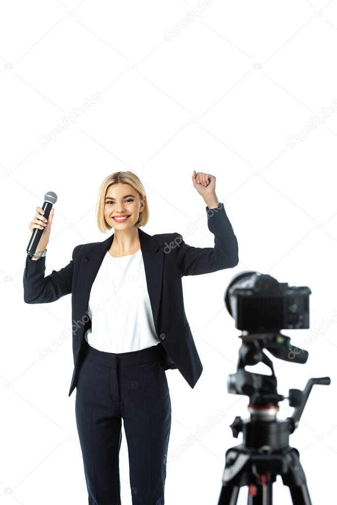 excited newscaster showing win gesture near digital camera on blurred foreground isolated on white