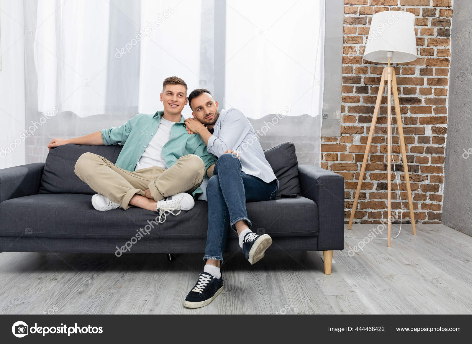 Cheerful Same Sex Couple Looking Away While Sitting Couch Home Stock Photo by ©AndrewLozovyi 444468422