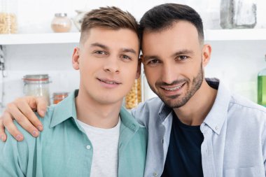 happy homosexual men looking at camera at home clipart