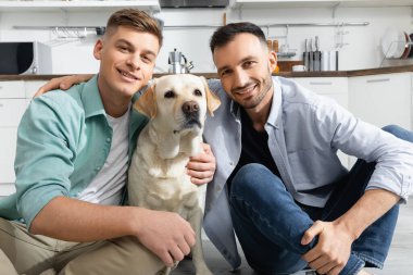 Evde köpekle gülümseyen neşeli homoseksüel erkekler.