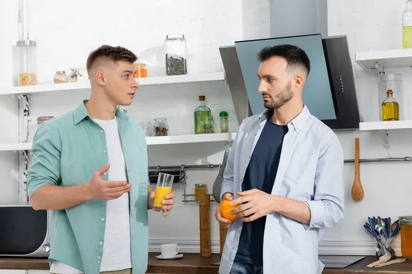 Homens Homossexuais Confusos Segurando Frutas Suco Laranja Cozinha — Fotografia de Stock