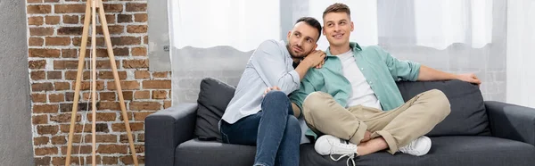同性伴侣一边坐在沙发上一边看一边在家里挂着横幅 — 图库照片