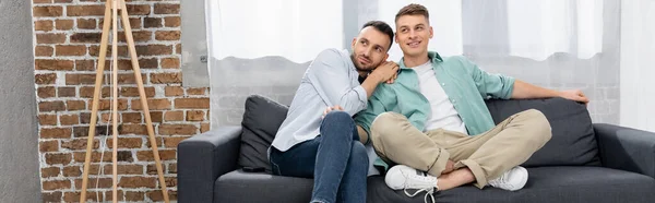 Cheerful Same Sex Couple Looking Away While Sitting Couch Home — Stock Photo, Image