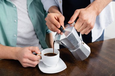 cropped view of homosexual man pouring coffee in cup near husband  clipart