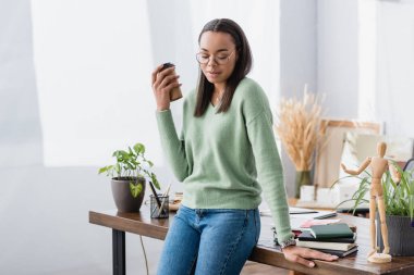 Genç Afro-Amerikan mimar gözleri kapalı elinde kağıt bardakla evdeki masanın yanında duruyor.