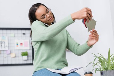 Afro-Amerikan iç mimar akıllı telefonla konuşurken renk paletine bakıyor. 