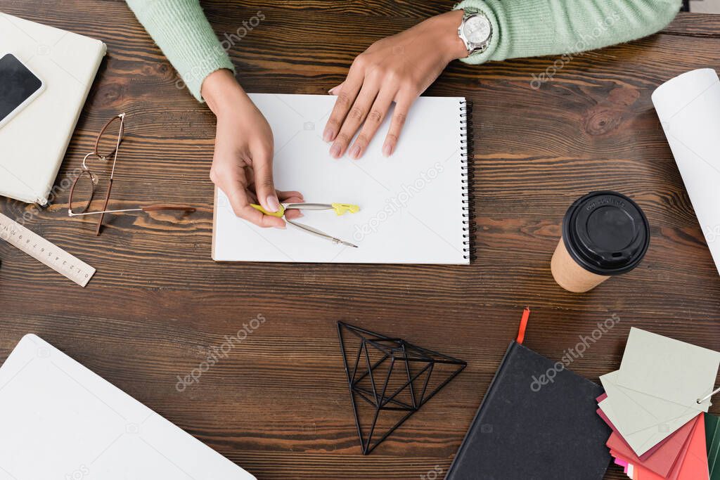 partial view of african american architect holding divider near sketchbook on desk at home