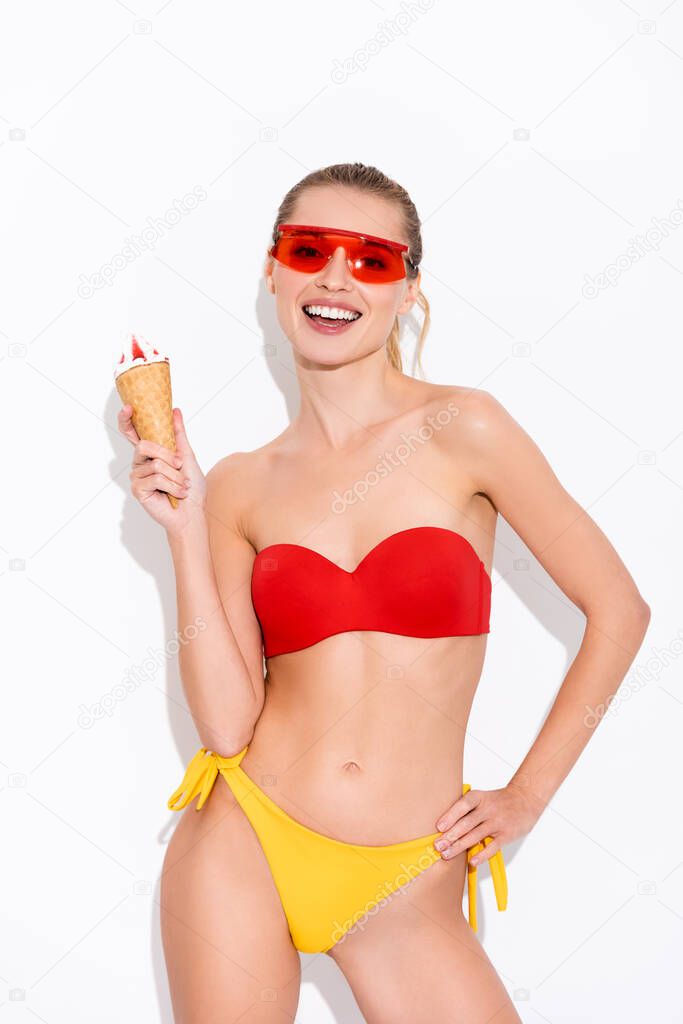 excited woman with hand on hip looking at camera while holding ice cream on white
