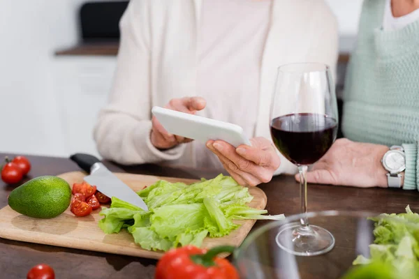 野菜の近くのスマートフォンをテーブルの上で使う年配の女性の — ストック写真