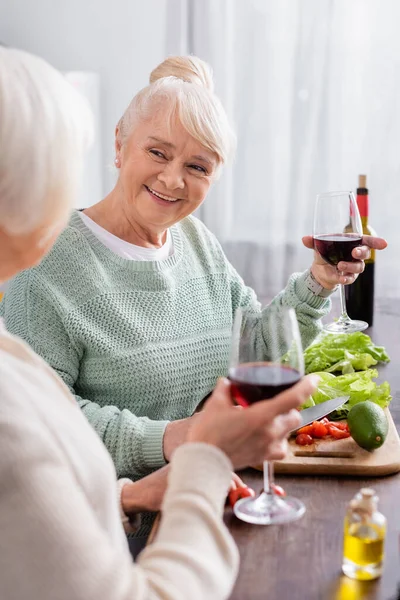 Feliz Anciana Sosteniendo Copa Vino Tinto Mirando Amigo Jubilado Primer —  Fotos de Stock