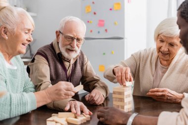 Mutlu ırklar arası emekliler evde odun blokları oynarken gülümsüyor.