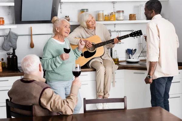 Sonriente Mujer Mayor Tocando Guitarra Acústica Cerca Amigos Jubilados Multiculturales —  Fotos de Stock