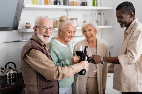 Happy Retired Man Holding Bottle Wine Senior Multicultural Friends Kitchen — Stock Photo, Image