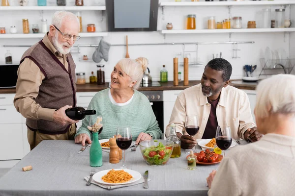 Retirado Hombre Gafas Verter Vino Tinto Vaso Cerca Feliz Interracial — Foto de Stock