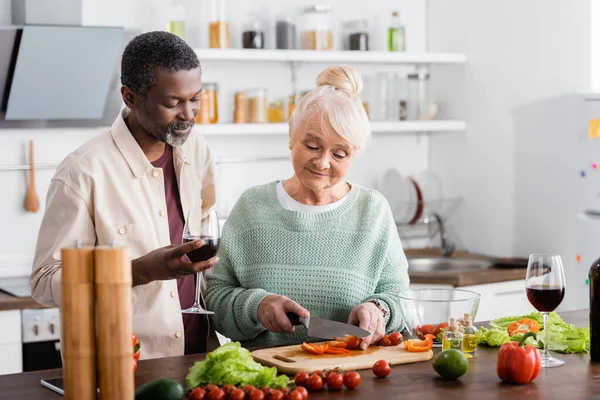 Senior Vrouw Snijden Bel Peper Buurt Van Afrikaanse Amerikaanse Man — Stockfoto