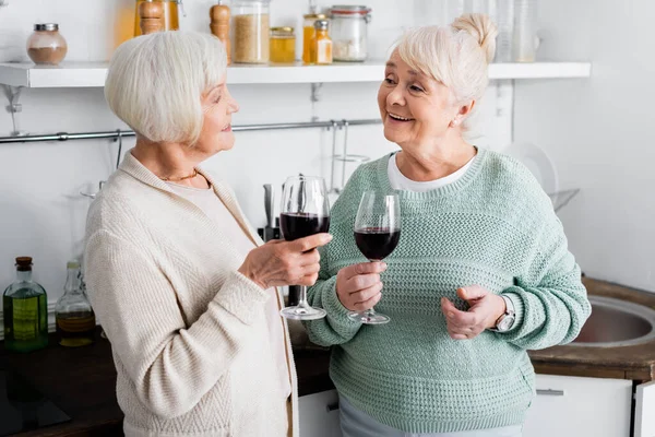 Happy Retired Women Holding Glasses Wine Looking Each Other Kitchen — Stock Photo, Image