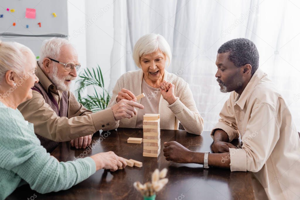 happy interracial pensioners playing tower wood blocks game at home