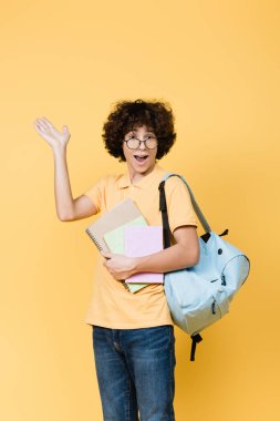 Not defterleri ve sırt çantasıyla mutlu bir genç, sarıya el izole edilmiş.