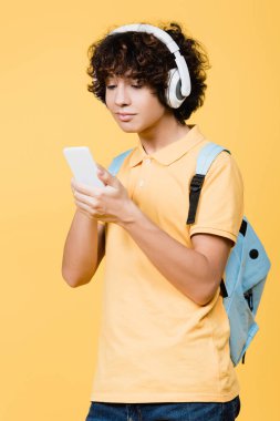 Kulaklıkla müzik dinleyen ve sarıda izole edilmiş cep telefonu kullanan genç bir çocuk.