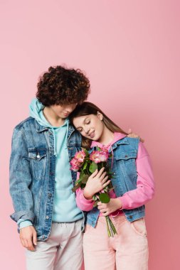 Sevgilisinin yanında çiçek tutan gülümseyen ergen pembe üzerinde izole. 