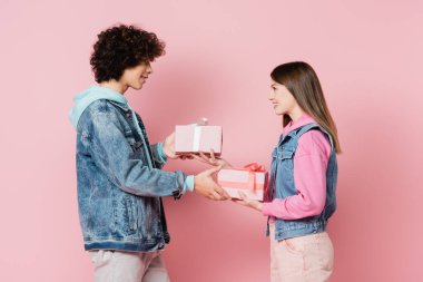 Gülümseyen gençlerin birbirlerine pembe renkte hediyeler vermesinin yan görünüşü 