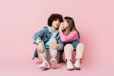 Pembe arka planda erkek arkadaşına fısıldayan bir genç.