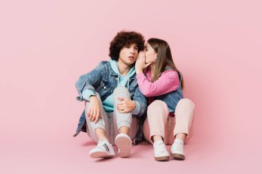 Teenager whispering to boyfriend on pink background clipart