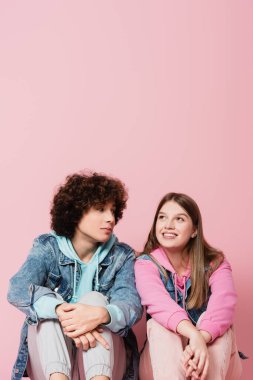 Kıvırcık ergen pembe arka planda gülümseyen kız arkadaşına bakıyor