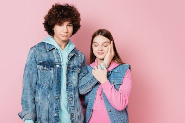 Kıvırcık çocuk pembe arka planda kız arkadaşının yüzünün yanında el ele tutuşuyor.