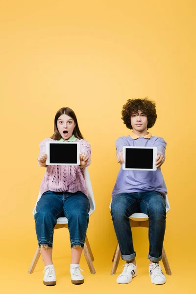 Excited Girl Showing Digital Tablet Blank Screen Friend Chair Yellow — Stock Photo, Image