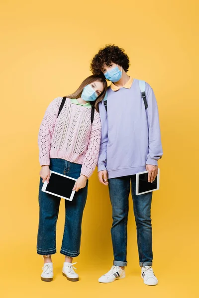 Adolescentes Con Máscaras Médicas Sosteniendo Tabletas Digitales Sobre Fondo Amarillo —  Fotos de Stock