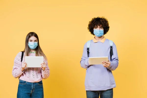 Tıbbi Maskeli Gençler Sarı Arka Planda Dijital Tabletler Taşıyorlar — Stok fotoğraf
