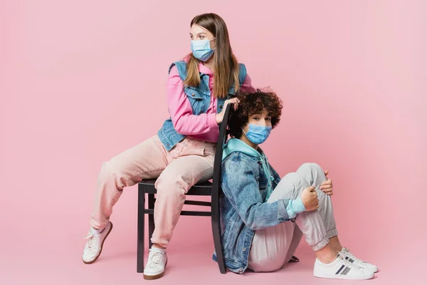 Curly Teenager Medical Mask Looking Camera Friend Chair Pink Background — Stock Photo, Image