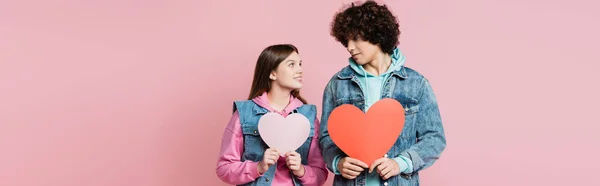 Sonriente Adolescente Sosteniendo Corazón Papel Mirando Novio Aislado Rosa Pancarta — Foto de Stock