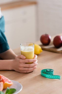 Kadının meyve suyu bardağının yanında kısmi görüntüsü ve ölçüm bandı, bulanık arkaplan