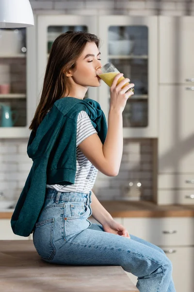 キッチンカウンターに座りながら新鮮なスムージーを飲む女の幸せ — ストック写真