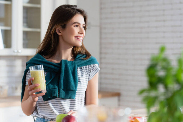 happy woman holding glass of fresh juice on blurred foreground in kitchen