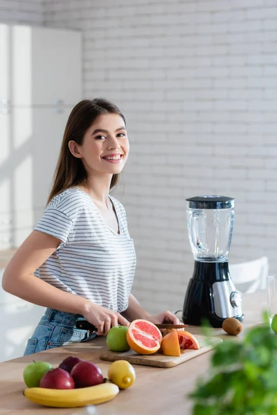 Glad Kvinna Tittar Kameran Samtidigt Skära Färska Frukter Suddig Förgrund — Stockfoto