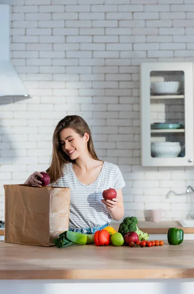 Mujer Alegre Sosteniendo Manzanas Jugosas Cerca Bolsa Papel Verduras Frescas — Foto de Stock